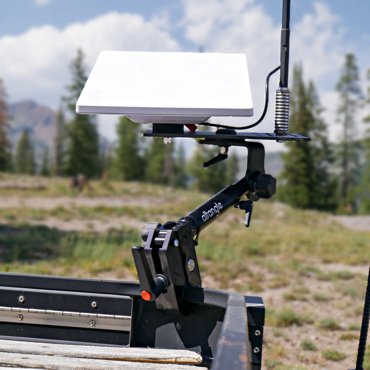 Starlink Mini on an Altangle Connect arm clamped to a UTV rail beside a whip antenna, mountain meadow behind